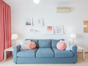 A living room with a blue sofa, two side tables with lamps, a red curtain, and wall-mounted air conditioning. - Boavista Charming Apartment by Interhome (Lagos)