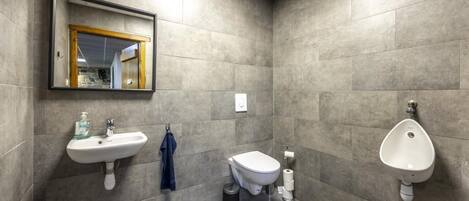A modern bathroom with a sink, toilet, and urinal, all with a minimalist design.