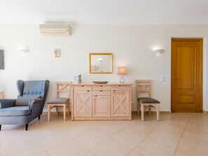 A living room with a sofa, two chairs, a wooden cabinet, a mirror, and a door. - Apartment  by Interhome (Lagos)