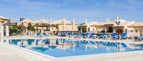 A swimming pool with lounge chairs and a building with a tiled roof.