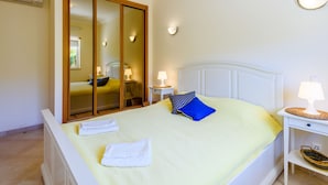 Een slaapkamer met een bed, nachtkastje met lamp, spiegel en een wandlamp.