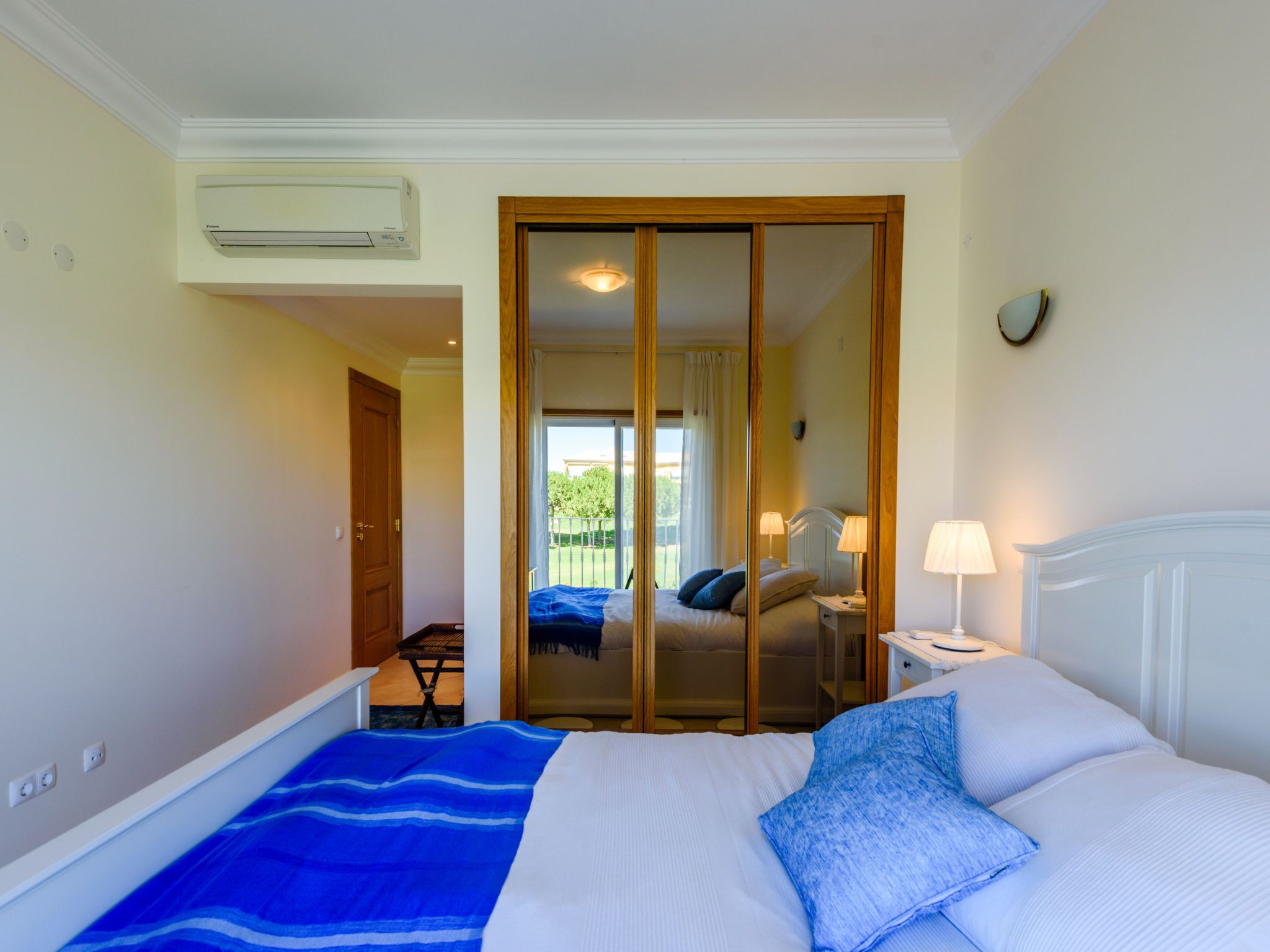 A hotel room with a bed, a nightstand, a lamp, a window with curtains, and a sliding door leading to a balcony.