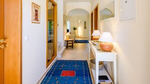 Een gang met een houten deur, een lijst met een afbeelding, een witte console tafel met lampen en een blauw tapijt met patroon.