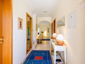 A hallway with a wooden door, a framed picture, a white console table with lamps, and a blue patterned carpet. - Vacation home  by Interhome (Lagos)