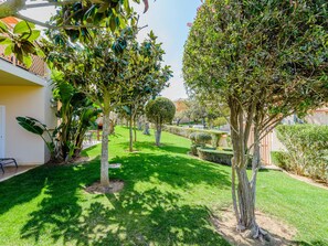 A well-maintained garden with various trees and shrubs, a neatly trimmed lawn, and a building with a balcony. - Casa Sunny Days - Boavista Resort by Interhome (Lagos)