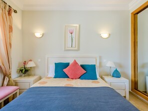 A hotel room with a bed, two nightstands, a night lamp, a wall-mounted picture, and a large mirror. - Casa Sunny Days - Boavista Resort by Interhome (Lagos)