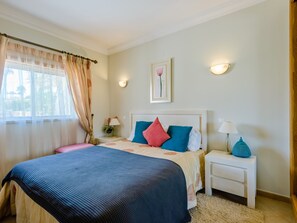 Ein Hotelzimmer mit einem großen Bett, zwei Nachttischen, einem Fenster mit Vorhängen, einem Wandbild und einer kleinen Lampe auf dem Nachttisch.