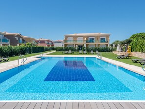 Une piscine dont le centre est d’un bleu limpide, entourée de chaises longues et bordée d’un bâtiment doté de balcons.