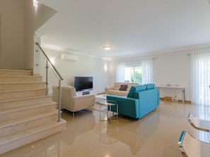 A modern living room with a staircase, a flat-screen TV, a teal sofa, and a dining area. - Vacation home  by Interhome (Lagos)