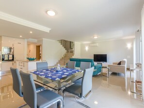 A modern living space with a glass dining table, a sofa, a TV, and a kitchen area. - Boavista Resort - Casa Belinda by Interhome (Lagos)