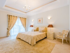 Ein Schlafzimmer mit einem großen Bett, Nachttischlampen, einem Nachttisch, einem Sessel und einer Pendelleuchte.