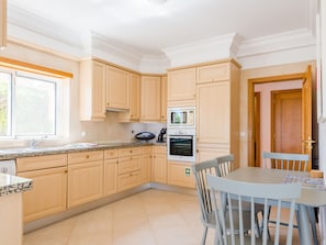 A modern kitchen with light wood cabinets, a granite countertop, a built-in oven, and a dining area with a table and chairs. - Casa Rosa at Boavista Resort by Interhome (Lagos)