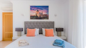 Ett hotellrum med en stor säng, två sängbord, en sänggavel och en tavla med ett slott på väggen.