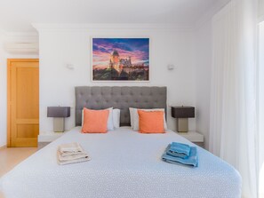Ein Hotelzimmer mit einem großen Bett, zwei Nachttischen, einem Kopfteil und einem Gemälde eines Schlosses an der Wand.