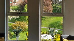 A room with a view of a well-maintained garden through a large window, a small table with a keyboard, and two chairs with cushions. - ⭐ Luxury 5-Star Apartment with Panoramic Pannett Park Views & Parking (Whitby)