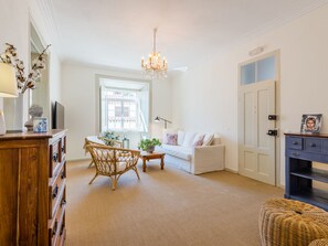 Ein geräumiges Wohnzimmer mit einem weißen Sofa, einem Korbstuhl, einem Holztisch und einer Pendelleuchte.