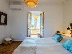 Ein Hotelzimmer mit Bett, Nachttisch, Lampe, Pflanze und Blick auf den Balkon.