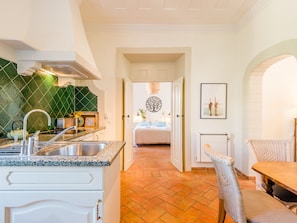 A modern kitchen with a sink, stove, and green backsplash. A dining area with a wicker chair and table is visible. - Apartment  by Interhome (Bensafrim)