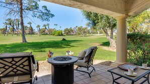 Um pátio com mobiliário externo, uma lareira e vista para um campo de golfe.