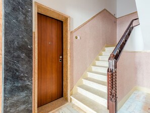 Eine Holztür mit schlichtem Griff, eine Treppe mit hölzernem Geländer und ein Marmorboden.