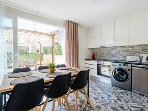A modern kitchen with a washing machine, a dining area with a table and chairs, and a view of the outside. - Apartment  by Interhome (Lisbon)