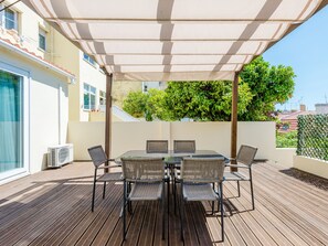 Een terras buiten met een tafel en stoelen, een pergola die schaduw biedt, en uitzicht op een stadsgezicht.