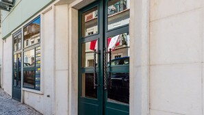 Un edificio con strada acciottolata, porte verdi e una finestra con tenda rossa.