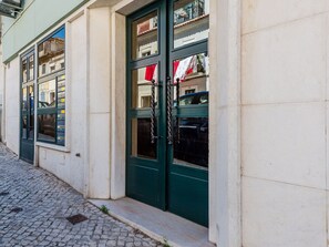 Ein Gebäude mit einer Kopfsteinpflasterstraße, grünen Türen und einem Fenster mit rotem Vorhang.