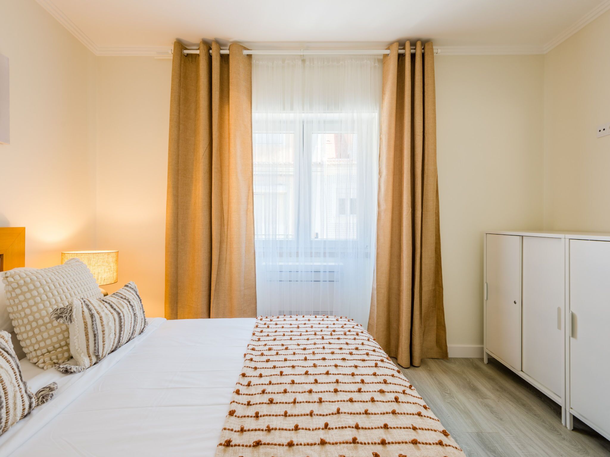 Een slaapkamer met een bed, gordijnen, een raam en een kledingkast.