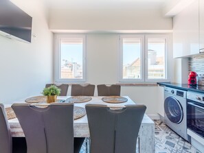 A modern kitchen with a built-in washing machine, a dining area with a table and chairs, and large windows with a city view. - Apartment  by Interhome (Lisbon)