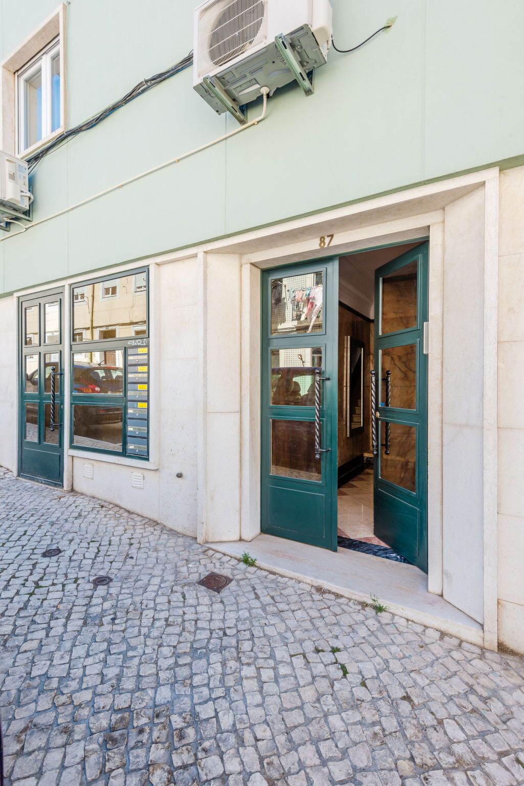 Un immeuble situé sur une rue pavée, avec une porte verte et le numéro « 87 » au-dessus.