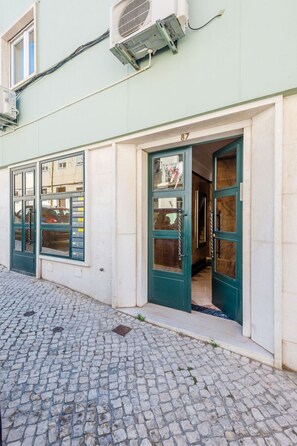 A building with a cobblestone street, a green door, and a number '87' above it. - Apartment  by Interhome (Lisbon)