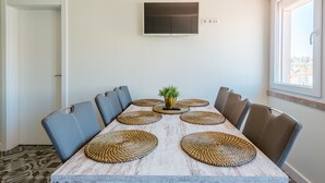 A dining area with a long table, chairs, woven placemats, a potted plant, and a mounted TV. - Apartment  by Interhome (Lisbon)