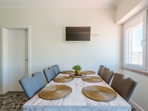 A dining area with a long table, chairs, woven placemats, a potted plant, and a mounted TV. - Apartment  by Interhome (Lisbon)