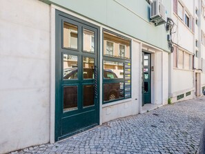 Un edificio con puerta verde y ventanas, calle adoquinada y unidad de aire acondicionado en la pared.