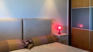 Een slaapkamer met een bed, een nachtkastje met een rode lamp en een houten garderobe.