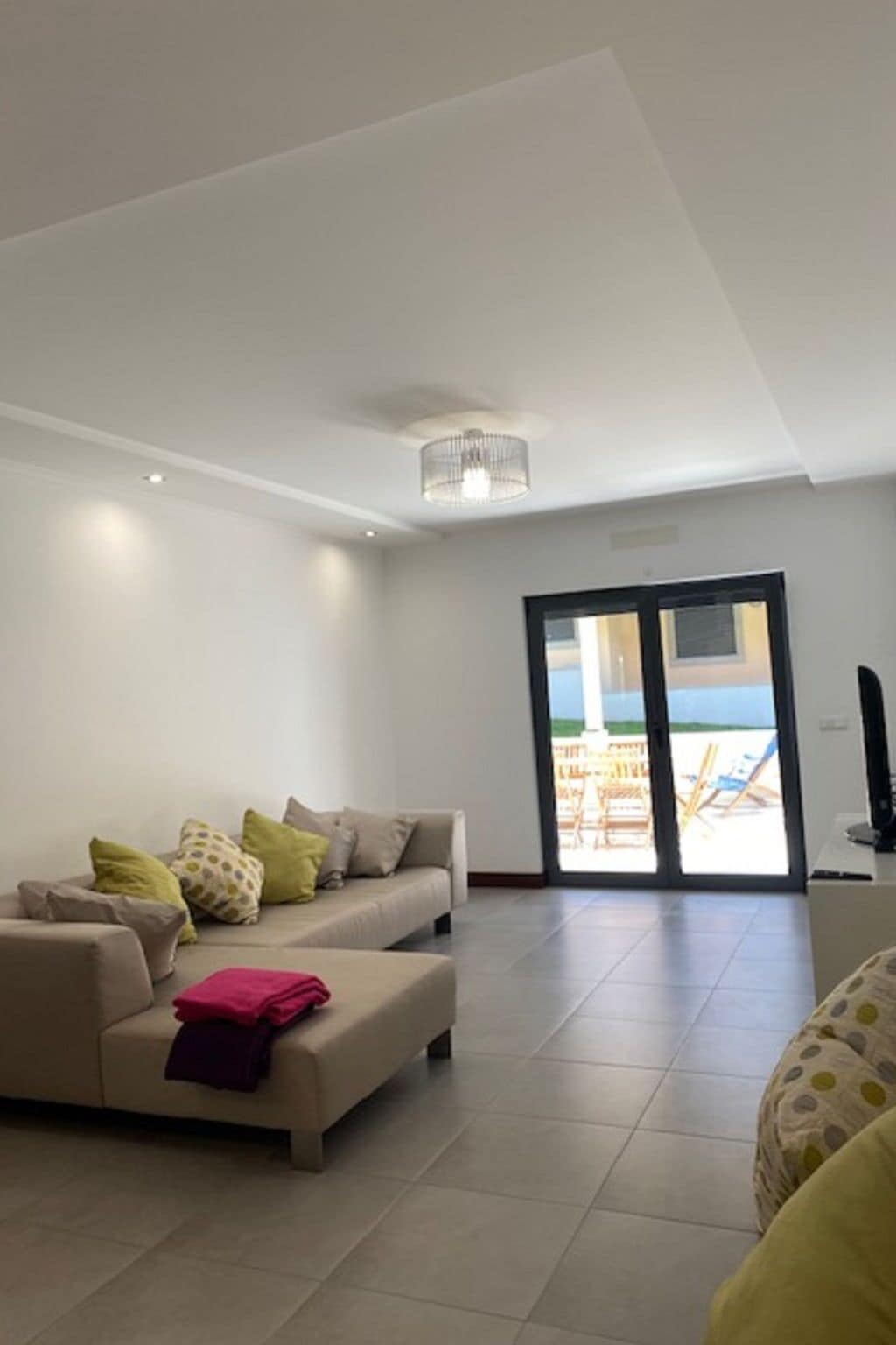 A modern living room with a sofa, a coffee table, and a television. There is a sliding glass door leading to an outdoor area.