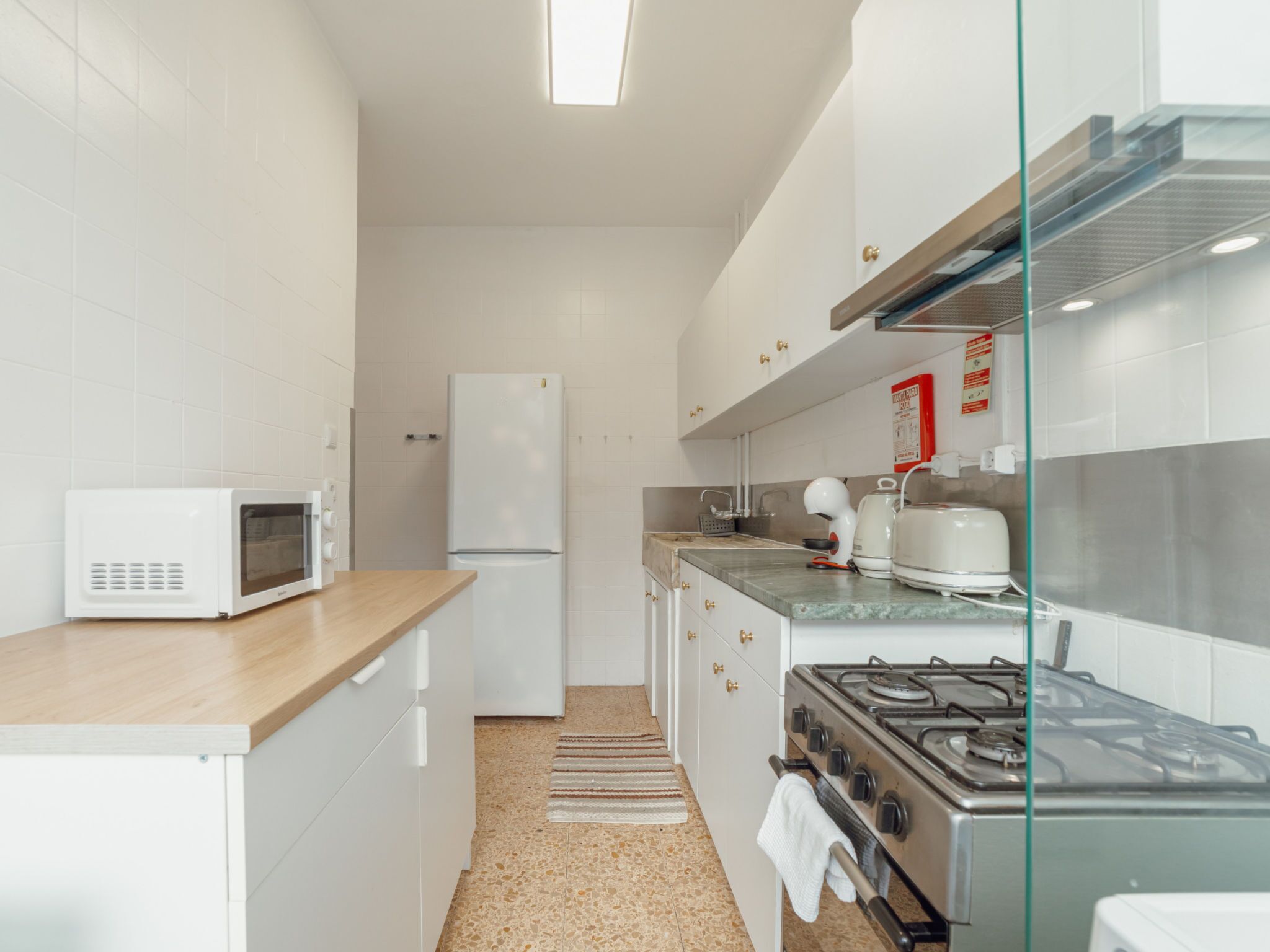 Cocina compacta con electrodomésticos blancos, microondas, refrigerador, estufa y cafetera.