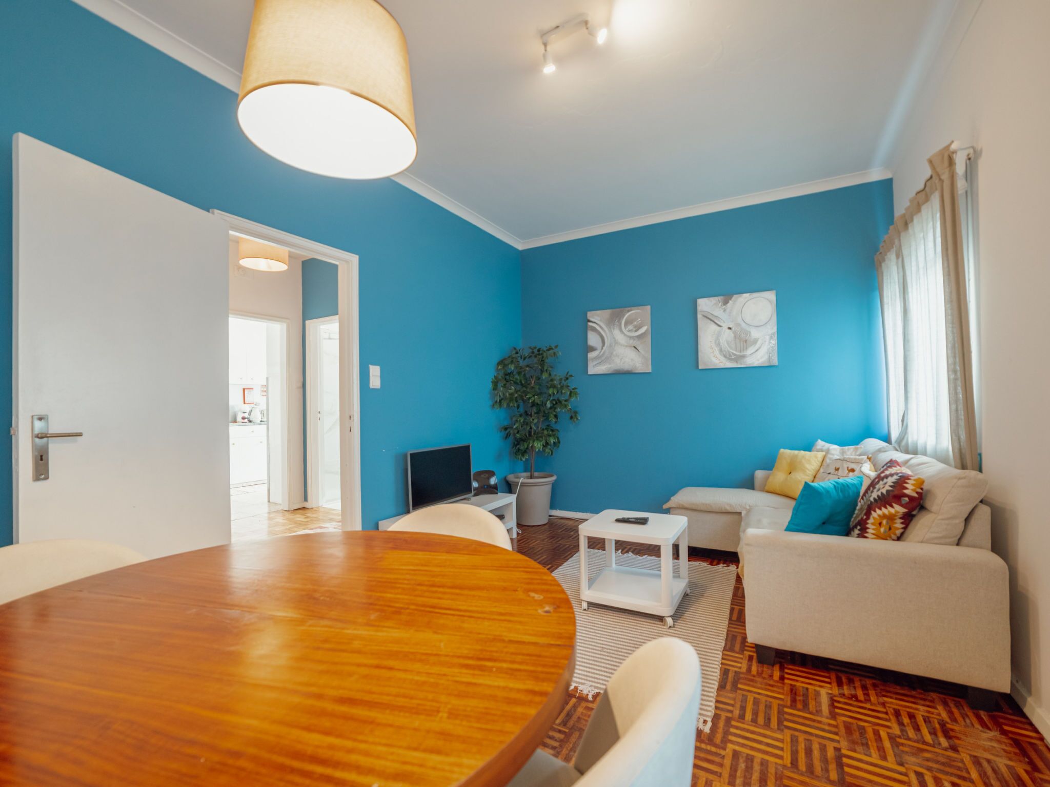 Una sala de estar moderna con una mesa de comedor de madera, un sofá, un televisor y una planta en maceta.