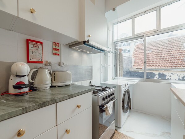 A kitchen with a gas stove, a washing machine, and a coffee maker.