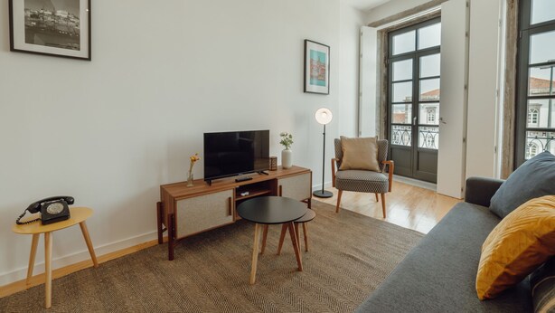 Ein Wohnzimmer mit einer Couch, einem Fernseher, einem kleinen Tisch, einem Sessel und einer Stehlampe.