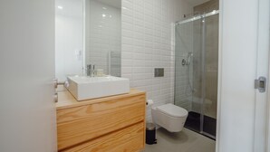 Ein modernes Badezimmer mit einem weißen Waschbecken, einer Holz-Kommode und einer Duschkabine.
