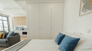 Ein Schlafzimmer mit Bett, Kissen, einer Couch und einer Küche im Hintergrund.
