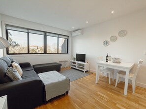 En moderne stue med sofa, fjernsyn, spisebord og stole.
