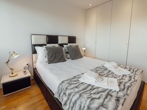 A neatly made bed with a marble-patterned blanket, a bedside lamp, and a folded towel on the bed. - DOWNTOWN STYLISH APARTMENT & GARAGE by VACATIONY by Interhome (Porto)