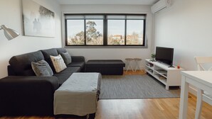 A modern living room with a black sofa, a grey rug, a flat-screen TV, and a dining table. - DOWNTOWN STYLISH APARTMENT & GARAGE by VACATIONY by Interhome (Porto)