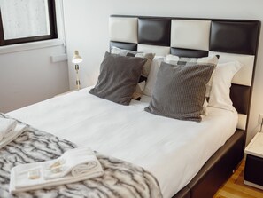 A neatly made bed with a marble-patterned blanket, a bedside lamp, and a nightstand with a lamp. - DOWNTOWN STYLISH APARTMENT & GARAGE by VACATIONY by Interhome (Porto)