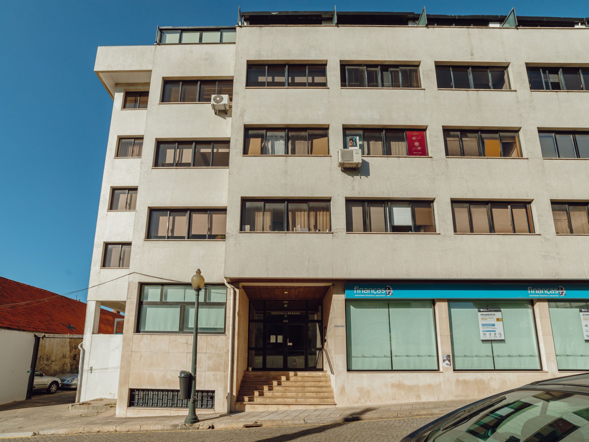 Ein mehrstöckiges Gebäude mit Eingangsbereich auf Straßenniveau und einer Treppe, die zum Eingang führt, sowie einer Beschilderung, die auf ein Geschäft im Erdgeschoss hinweist.