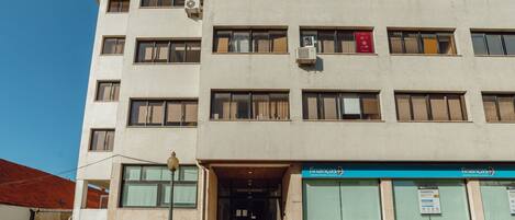 Un edificio de varios pisos con entrada a nivel de calle, una escalera que lleva a la entrada y un letrero que indica un negocio en la planta baja.