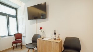 Una habitación moderna con televisión de pantalla plana en la pared, un escritorio de madera con un florero y dos sillas negras.